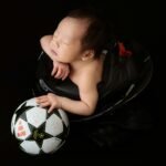 Charming newborn baby peacefully sleeping with a soccer ball, showcasing a unique and heartwarming black background capture.